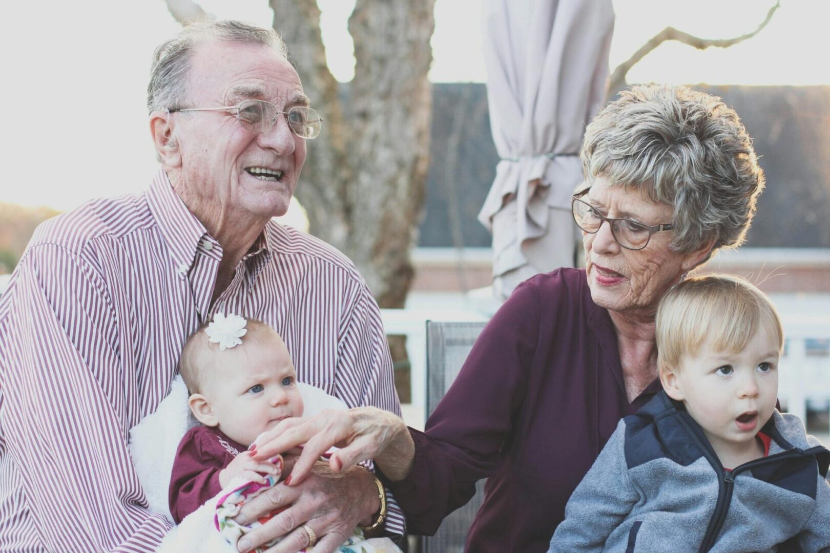An older couple holding a baby and talking to another elderly man.
