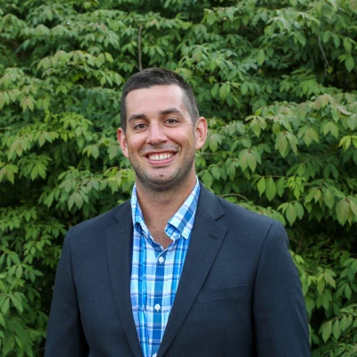 A man in a suit standing next to some bushes