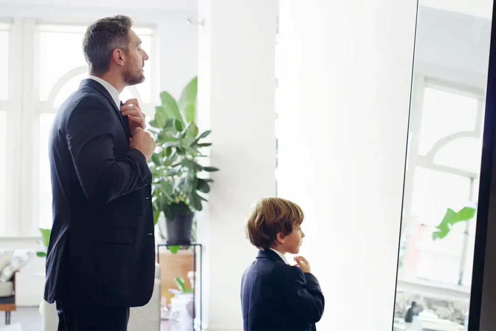 dad in suit showing son how to tie a tie