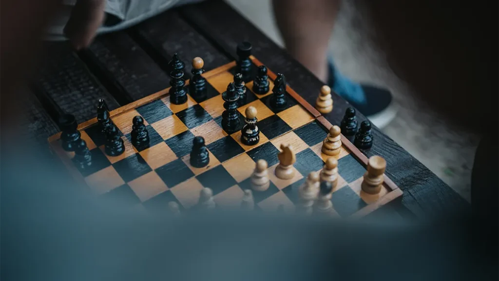 Close up of chess board, with camera hovering over someone shoulder. Subject's shoulder is out focused and in the foreground